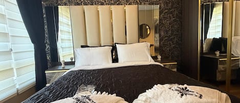 A hotel room with a large bed, a headboard with vertical panels, a bedside table with a lamp, and a mirror on the wall.