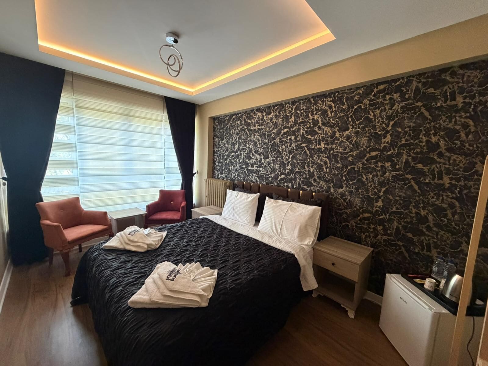 A hotel room with a large bed, a nightstand, a red armchair, and a marble-patterned wall.