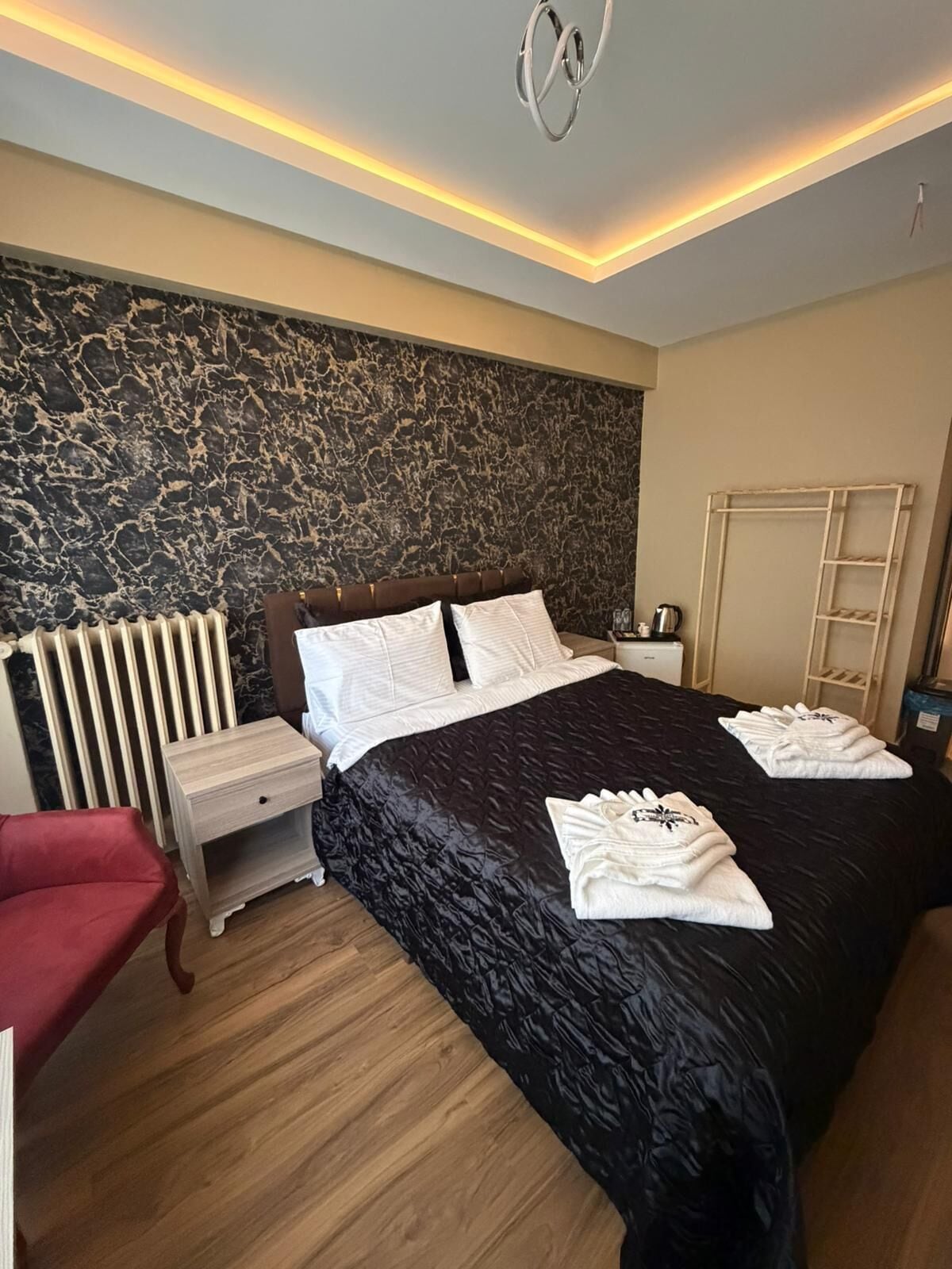 Een hotelkamer met een groot bed, een rode stoel, een houten nachtkastje, een radiator en een kledingkast.