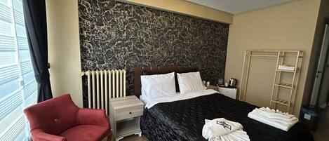 A modern hotel room with a large bed, a red armchair, a bedside table, and a radiator.