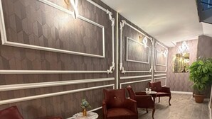 Una habitación con piso de madera oscura, sillas tapizadas en rojo, una pequeña mesa redonda con un florero y paneles decorativos en la pared.