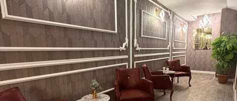 Una habitación con piso de madera oscura, sillas tapizadas en rojo, una pequeña mesa redonda con un florero y paneles decorativos en la pared.