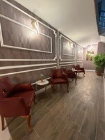 Una habitación con piso de madera oscura, sillas tapizadas en rojo, una pequeña mesa redonda con un florero y paneles decorativos en la pared.