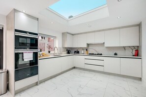Una cocina moderna con tragaluz, armarios blancos y suelo de mármol.