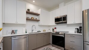A modern kitchen with stainless steel appliances, white cabinetry, and a patterned rug. - NEW 2BR Victoria Suite: Family, Pet, Work-Friendly (Colwood)