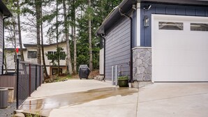 A residential driveway leading to a garage, with a covered grill and a stone wall. - NEW 2BR Victoria Suite: Family, Pet, Work-Friendly (Colwood)