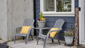 Two Adirondack chairs with yellow cushions, a small table, and potted plants on a porch with a 'WELCOME' sign. - NEW 2BR Victoria Suite: Family, Pet, Work-Friendly (Colwood)
