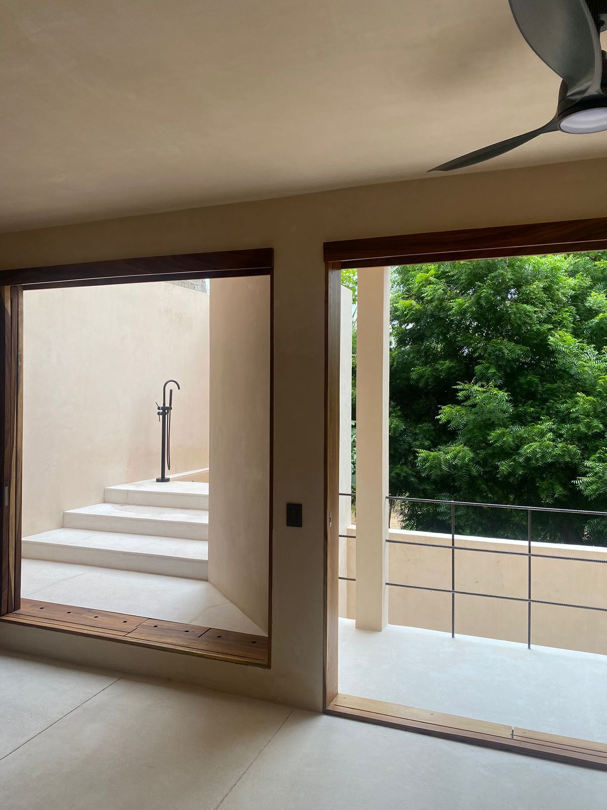 A spacious room with a large sliding glass door leading to a balcony with a view of lush greenery.