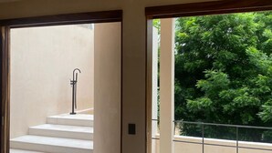 Une pièce spacieuse dotée d’une grande porte-fenêtre coulissante qui donne sur un balcon offrant une vue sur une végétation luxuriante.