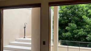 A spacious room with a large sliding glass door leading to a balcony with a view of lush greenery.