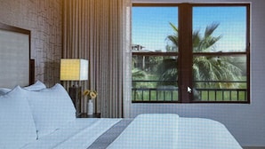 A hotel room with a large bed, a nightstand with a lamp, a vase with flowers, and a window with a view of palm trees.