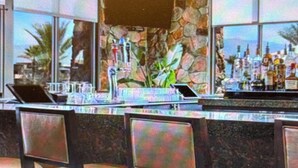 A bar area with a stone wall, a large window, and a view of palm trees.