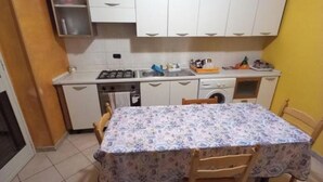Una cucina compatta con mobili bianchi, pavimento piastrellato e un tavolo da pranzo con sedie.