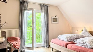 A bedroom with a bed, a chair, a desk, a radiator, a window with curtains, and a picture on the wall.