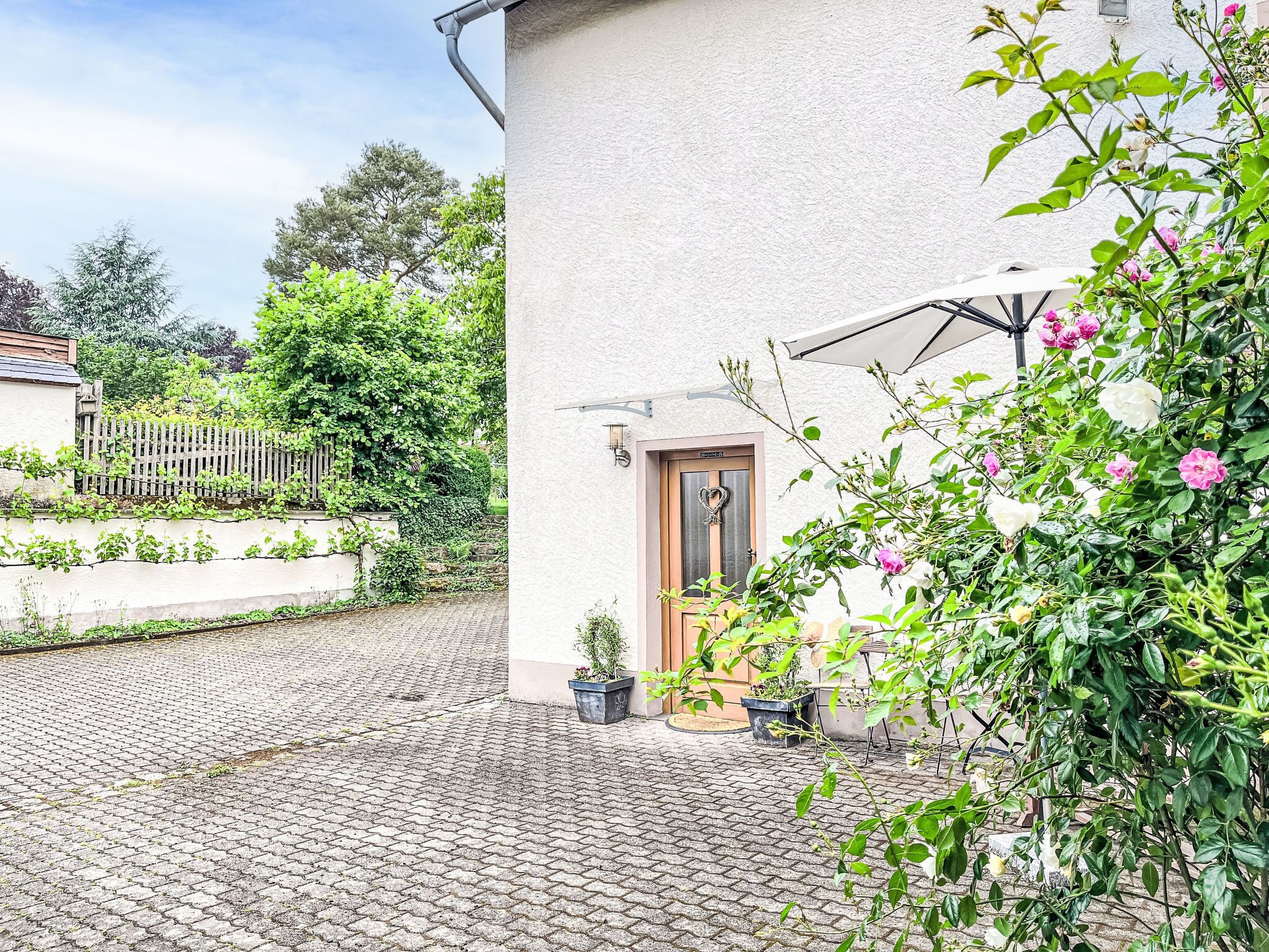 A paved courtyard with a white building, a wooden door, and potted plants.