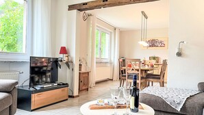 A cozy living room with a TV, a dining area with chairs and a table, and a sofa.