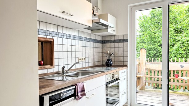 A modern kitchen with a built-in oven, a dishwasher, and a large window leading to a patio.