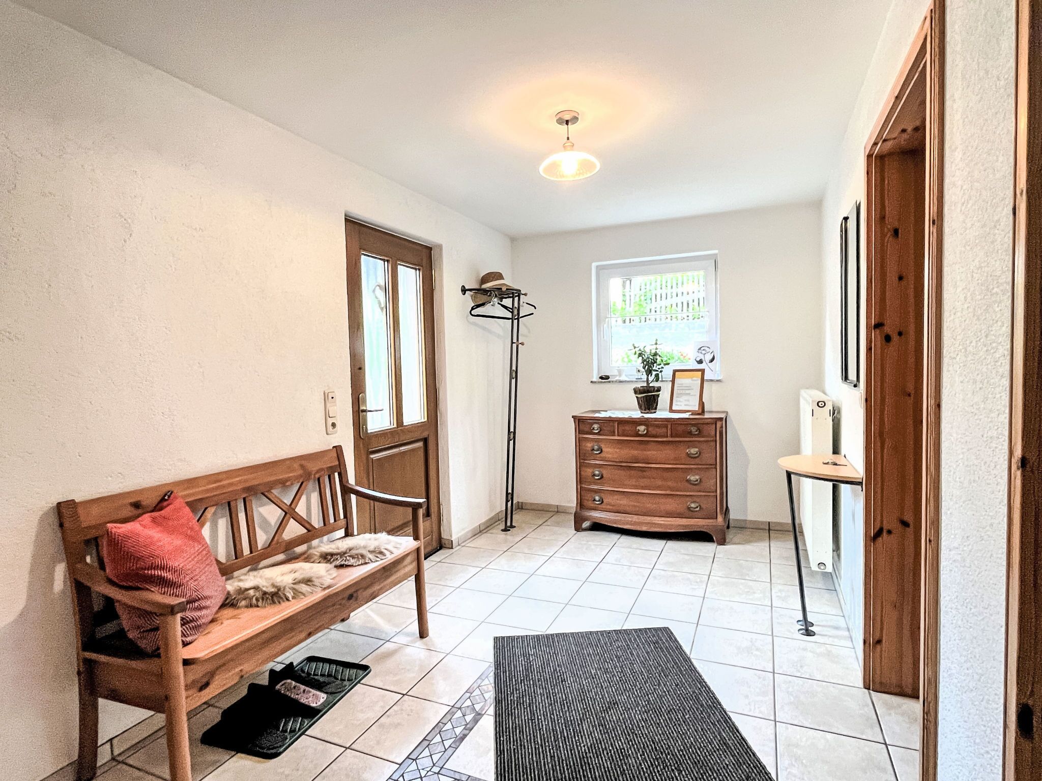Een kamer met een houten bankje, een kaptafel, een radiator, een raam en een deur.
