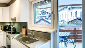 A modern kitchen with stainless steel appliances, a large window, and a view of traditional buildings outside. - Apartment Dala by Interhome (Leukerbad)