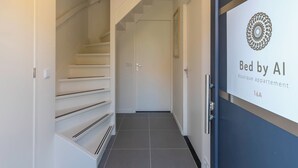 A modern hallway with a staircase, a door, and a sign for 'Bed by AI Boutique appartement 144A'.