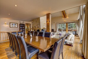 Een ruime eetruimte met een lange houten tafel en lederen stoelen, een stenen openhaard en een gezellige zithoek met een bank en fauteuils.