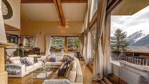 A spacious living room with a large window offering a mountain view, a cozy fireplace, and a wooden ceiling.