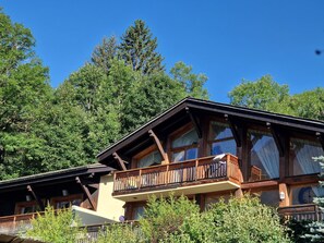 Een houten chalet met balkon, omringd door dicht bos.