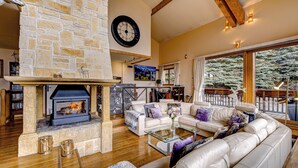 A spacious living room with a stone fireplace, leather sofa, and a large window overlooking a snowy landscape.