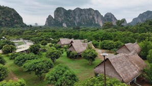 A rural village with thatched-roof huts surrounded by lush greenery and mountains in the background. - NUBDAO 168 Homestay (Lan Sak)