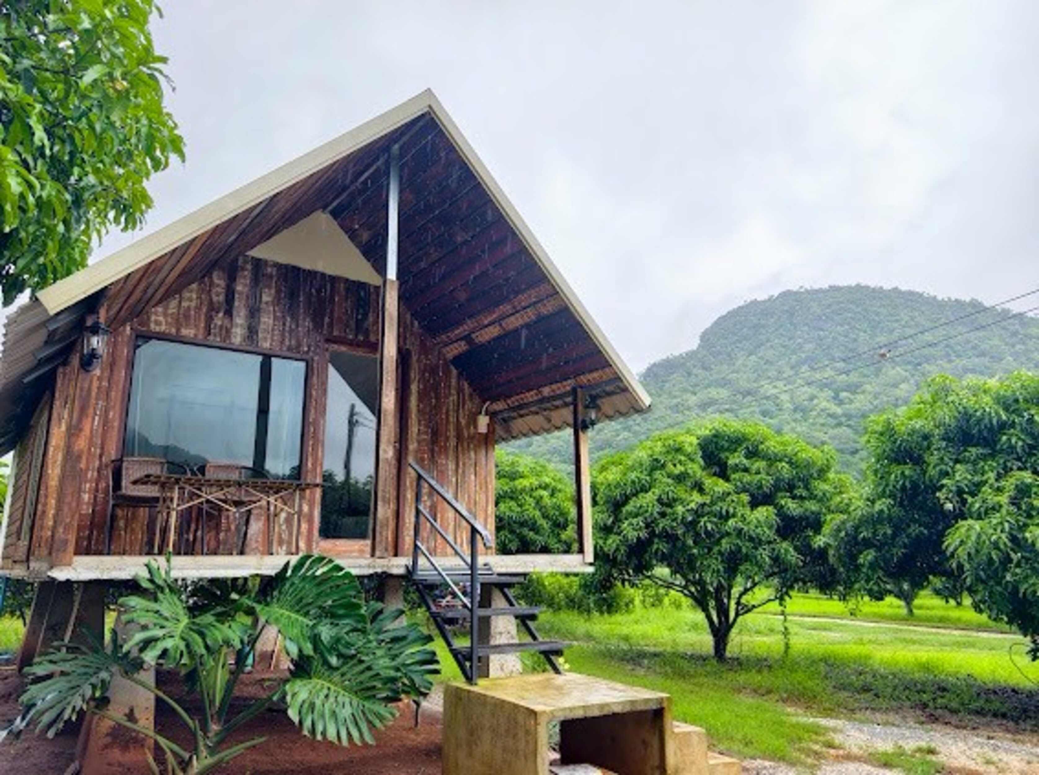 A wooden cabin with a large window, a staircase, and a view of a lush green landscape.