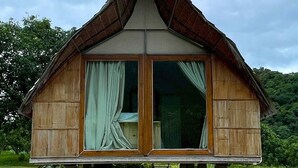 A small wooden house with a thatched roof, large windows with curtains, and a table under the porch. - NUBDAO 168 Homestay (Lan Sak)