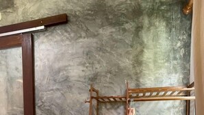 A corner room with a wooden shelf unit against a textured wall, a wooden chair, and a wooden door frame. - NUBDAO 168 Homestay (Lan Sak)