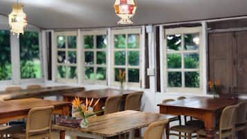A spacious dining area with wooden tables and chairs, large windows, and hanging pendant lights.