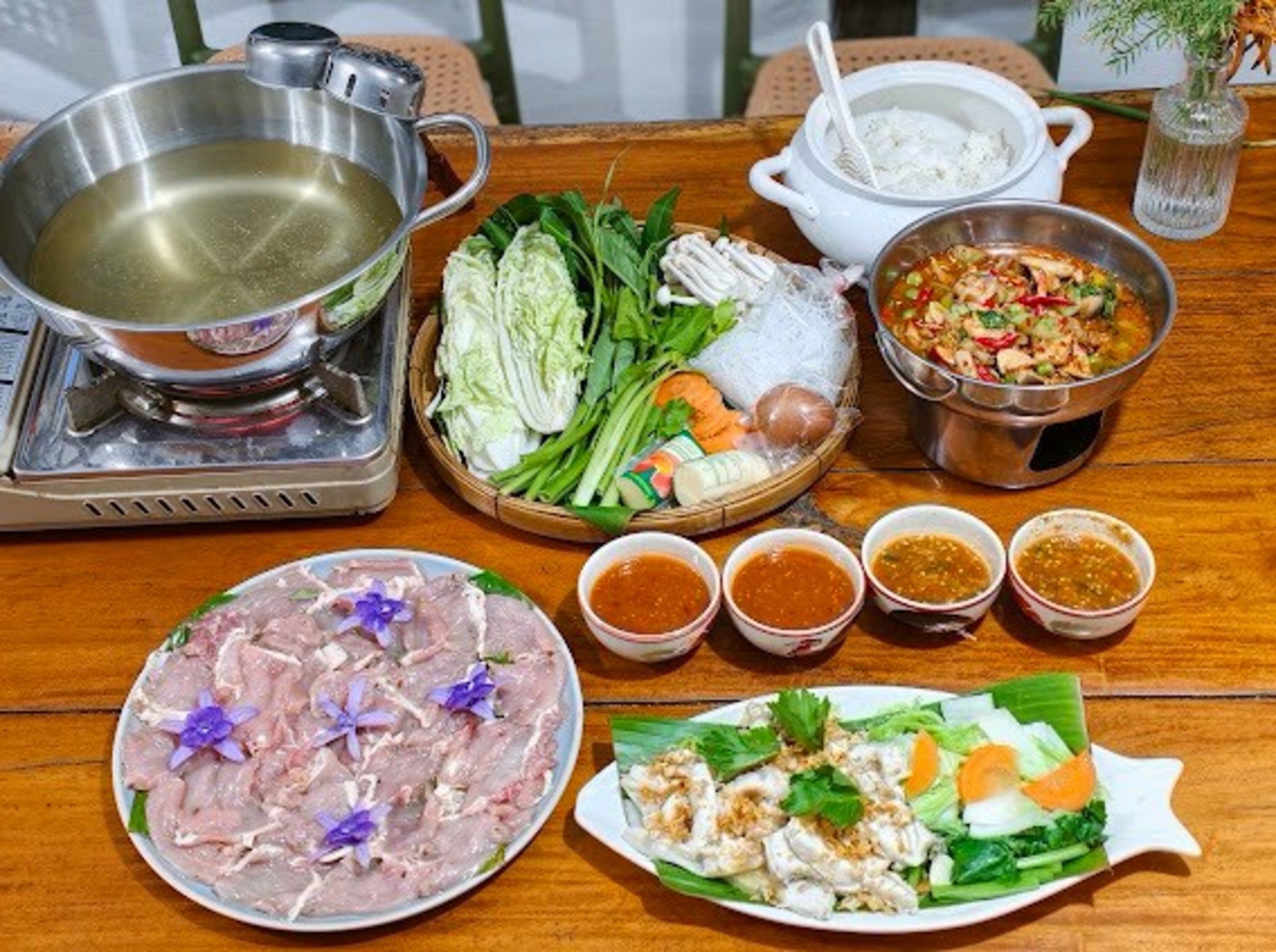 A table with a variety of dishes, including a hot pot, fresh vegetables, and several small bowls of sauces.