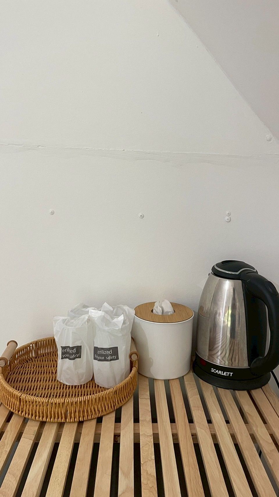 Una kitchenette con un hervidor de acero inoxidable, una bandeja de mimbre con dos bolsas etiquetadas como 'erilized you safety' y un recipiente blanco con tapa.