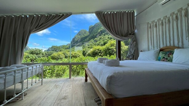 A bedroom with a large bed, a view of lush greenery and mountains, and a balcony with a railing. - NUBDAO 168 Homestay (Lan Sak)