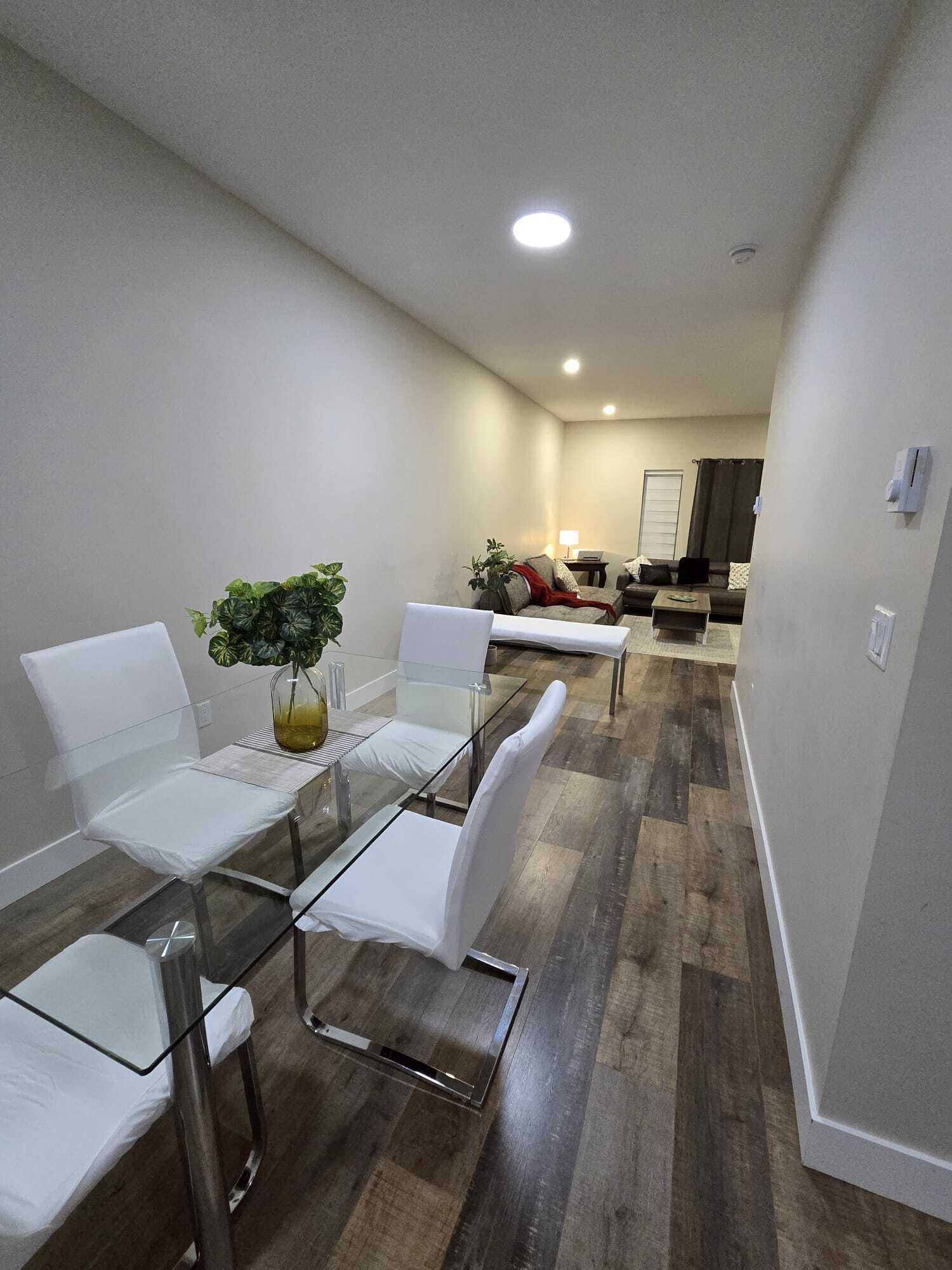 Un salon moderne avec une table à manger en verre, des chaises blanches et un canapé.