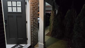 A residential garage door with a welcome mat, a brick wall, and a covered driveway. - 3-bedroom townhome in enchanting Abbotsford with AC (Abbotsford)