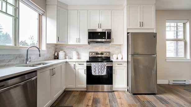 A modern kitchen with white cabinets, stainless steel appliances, and a wooden floor. - 3-bedroom townhome in enchanting Abbotsford with AC (Abbotsford)