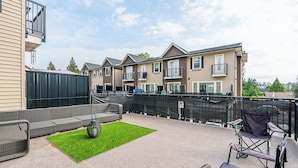 A rooftop patio with outdoor seating, a small lawn area, and a view of residential buildings in the background. - 3-bedroom townhome in enchanting Abbotsford with AC (Abbotsford)