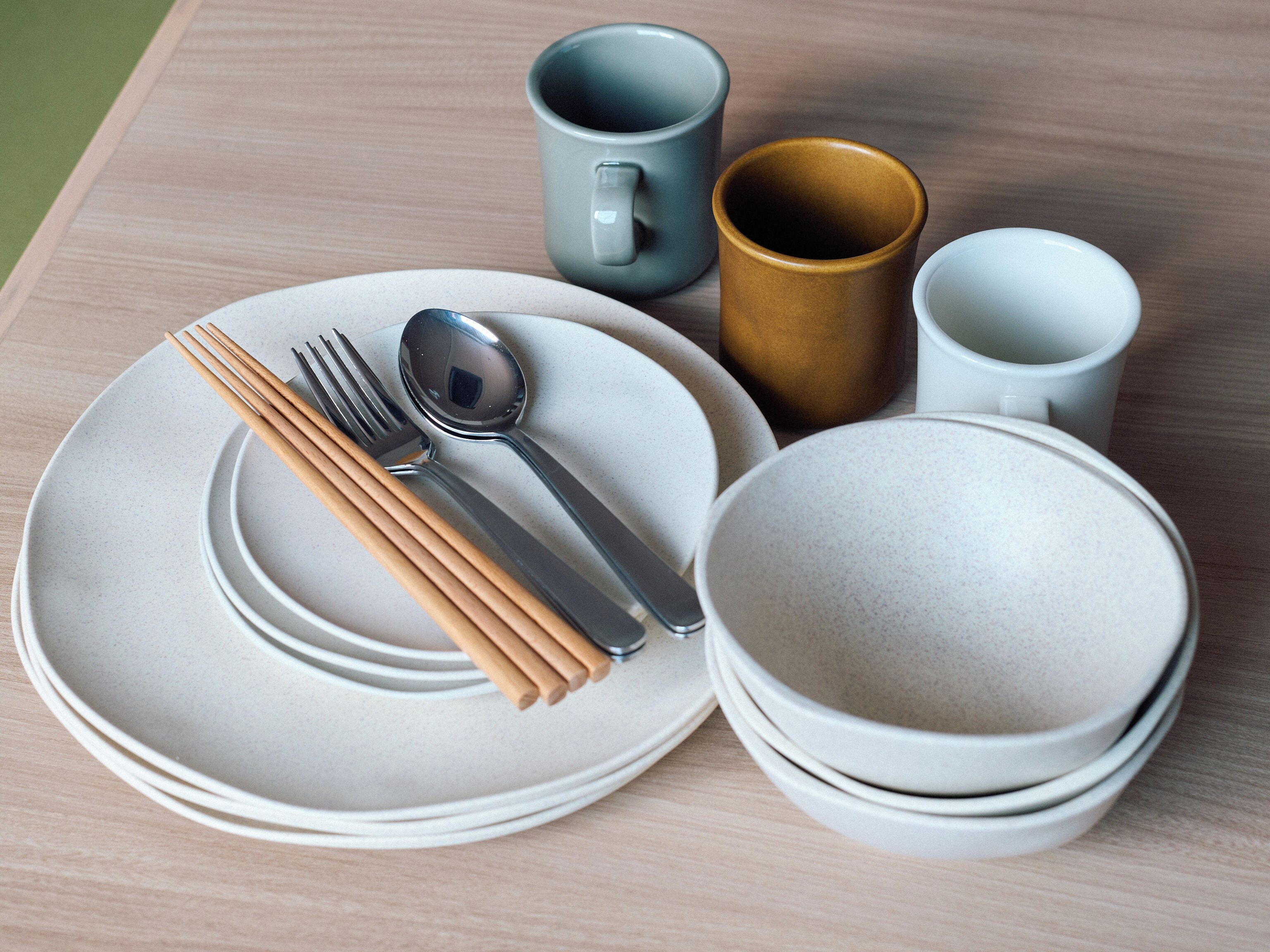 Une table dressée avec des assiettes, des bols, une cuillère, des baguettes et deux tasses.