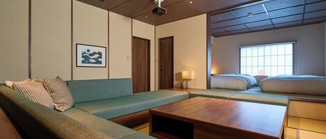 A modern hotel room with a sofa, a wooden coffee table, a bed with a view, and a ceiling with recessed lighting.