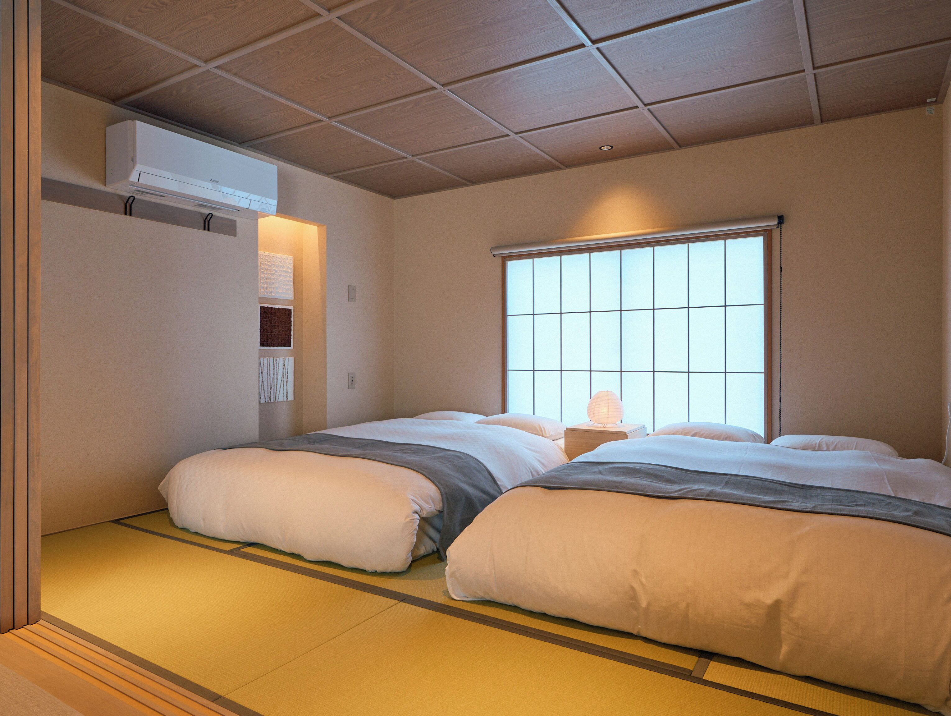 Hotellihuone, jossa on perinteinen japanilainen tatamimatto lattiana, suuri ikkuna, josta on näkymä, sekä yöpöytä, jossa on lamppu.