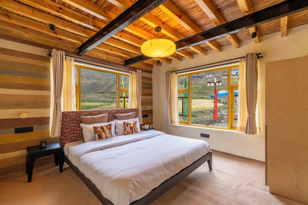 A bedroom with a large bed, wooden ceiling beams, and a view of the outdoors.