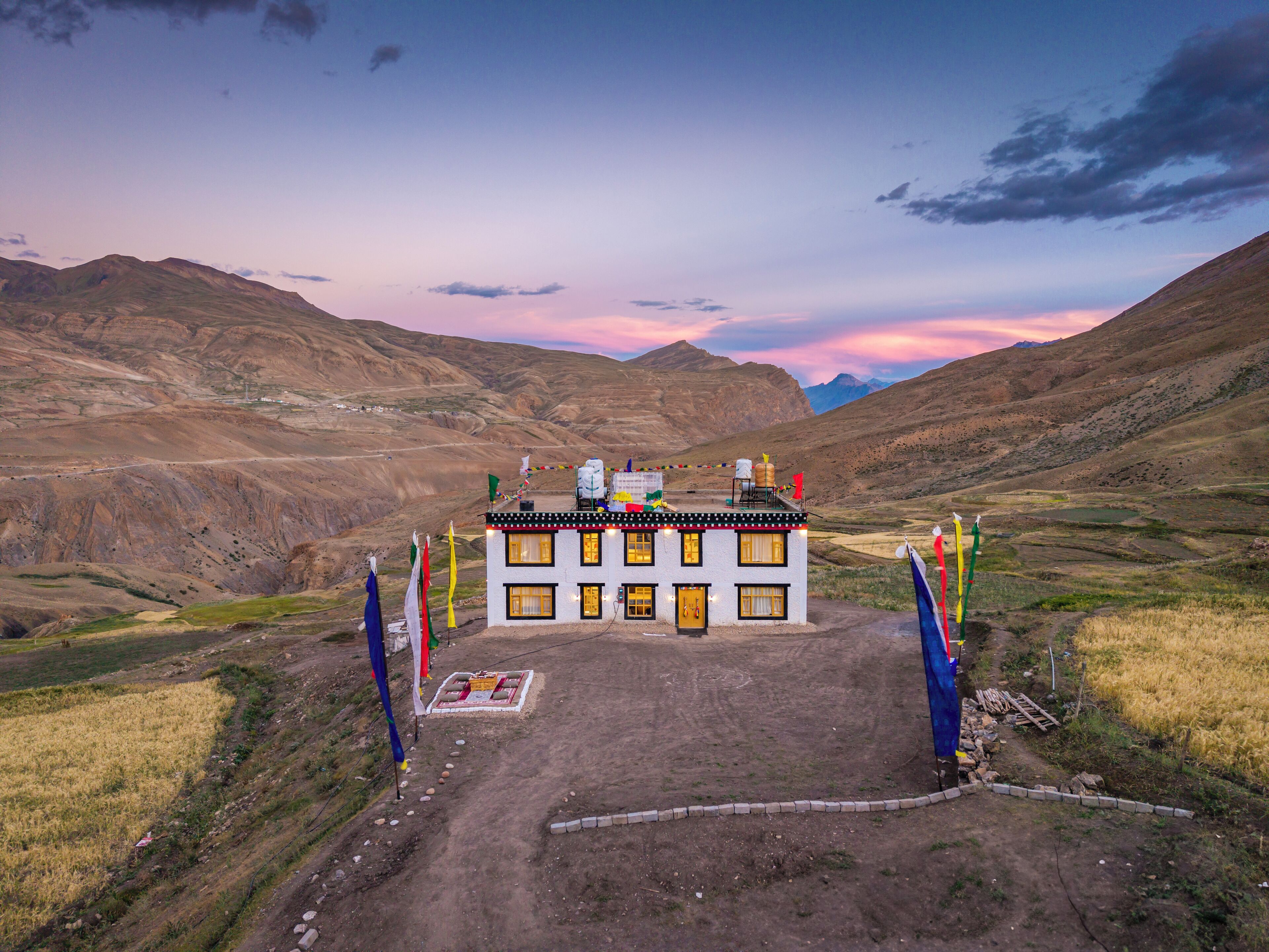Un edificio con múltiples ventanas y techo plano, rodeado de banderas y un sendero de tierra que lleva a él.
