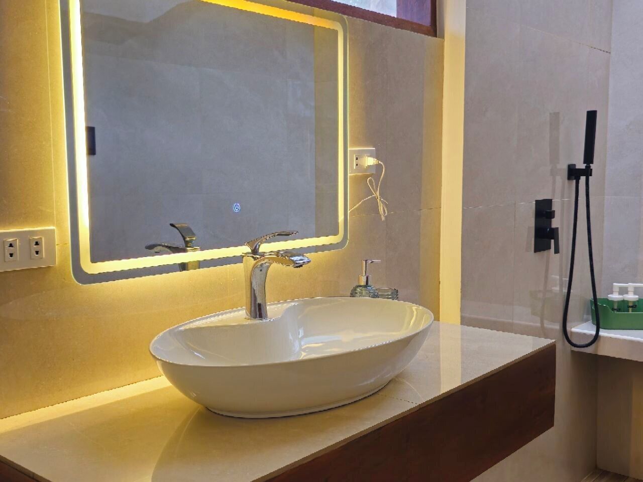 A modern bathroom with a large oval sink, a mirror with a lighted frame, and a handheld showerhead.
