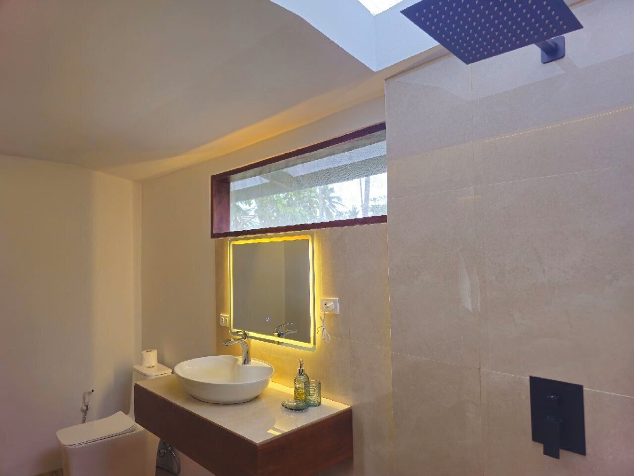Un baño moderno con tragaluz, un espejo grande, un lavabo blanco y un perchero para toallas.