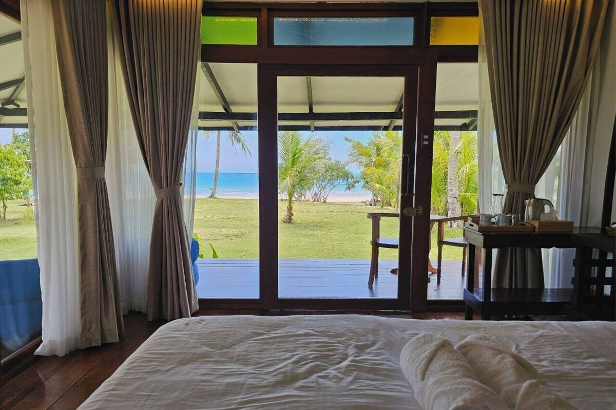 Un dormitorio con cama, cortinas y vistas a una playa y palmeras.
