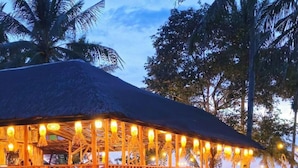 A wooden structure with a thatched roof, surrounded by tropical plants and palm trees. - BAIBAI (San Vicente)