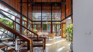 Un intérieur spacieux avec un escalier en bois, un coin repas comprenant une table et des chaises, et de grandes fenêtres offrant une vue sur l’extérieur.